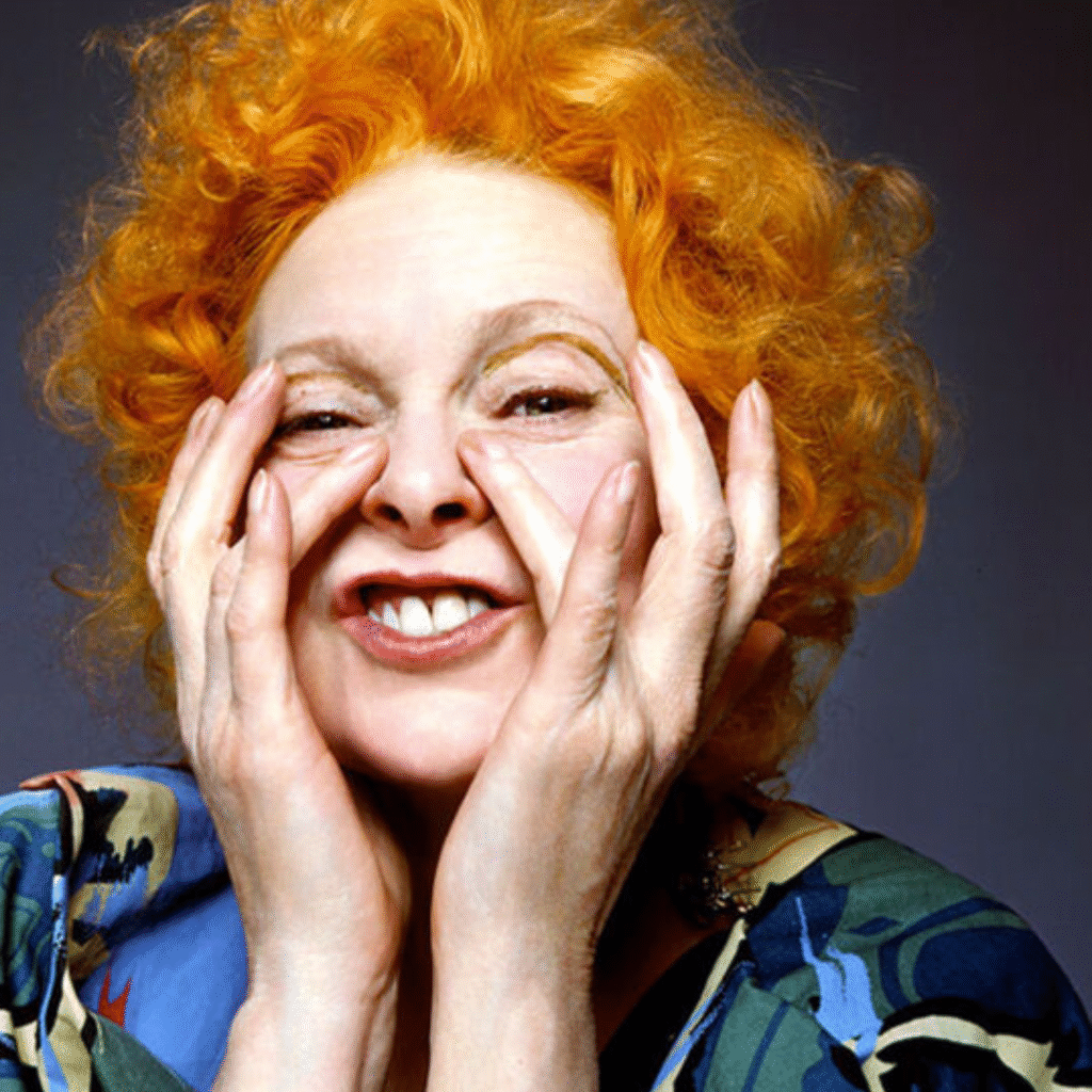 Woman with bright orange curly hair makes a playful face, pressing her cheeks with her hands.